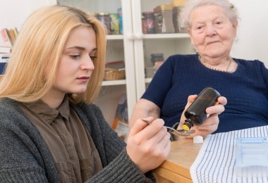 Eine junge Frau pflegt eine ältere Frau indem sie Medizin portioniert. 