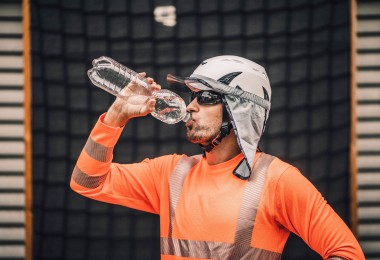 Ein Arbeitnehmer trägt Kleidung zum Schutz gegen Hitze und trinkt Wasser aus einer Flasche.