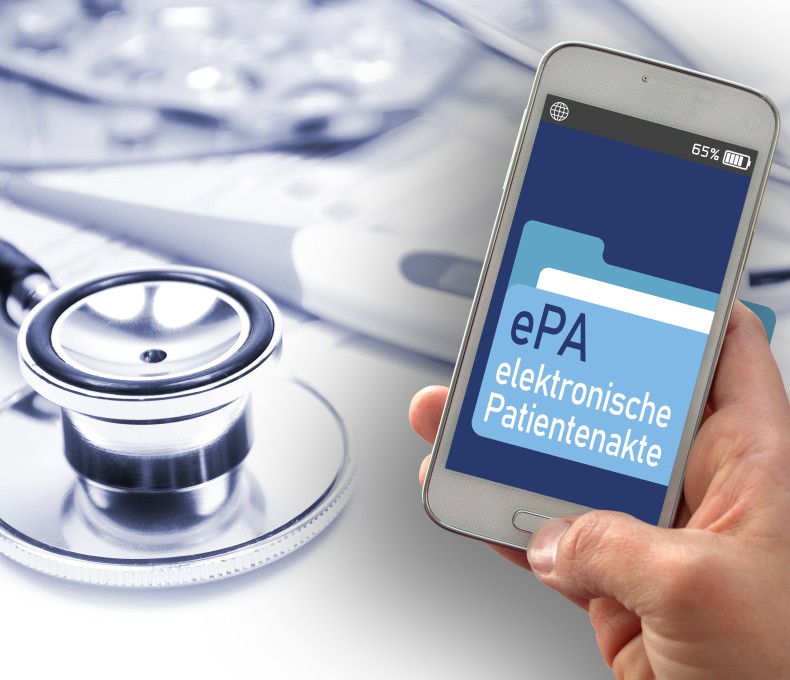 Das Bild zeigt eine Hand, die ein Smartphone hält. Auf dem Bildschirm des Smartphones ist eine Anwendung mit der Aufschrift „ePA – elektronische Patientenakte“ zu sehen. Im Hintergrund liegen medizinische Utensilien, wie ein Stethoskop und Tablettenblister.